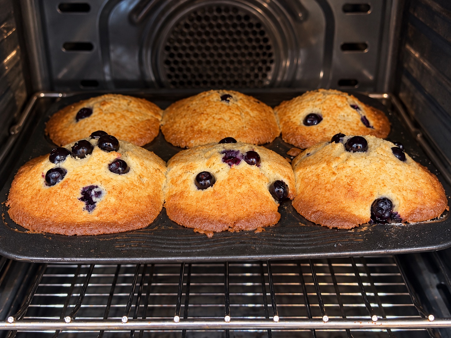 Six golden blueberry muffins baking in a jumbo muffin tray.